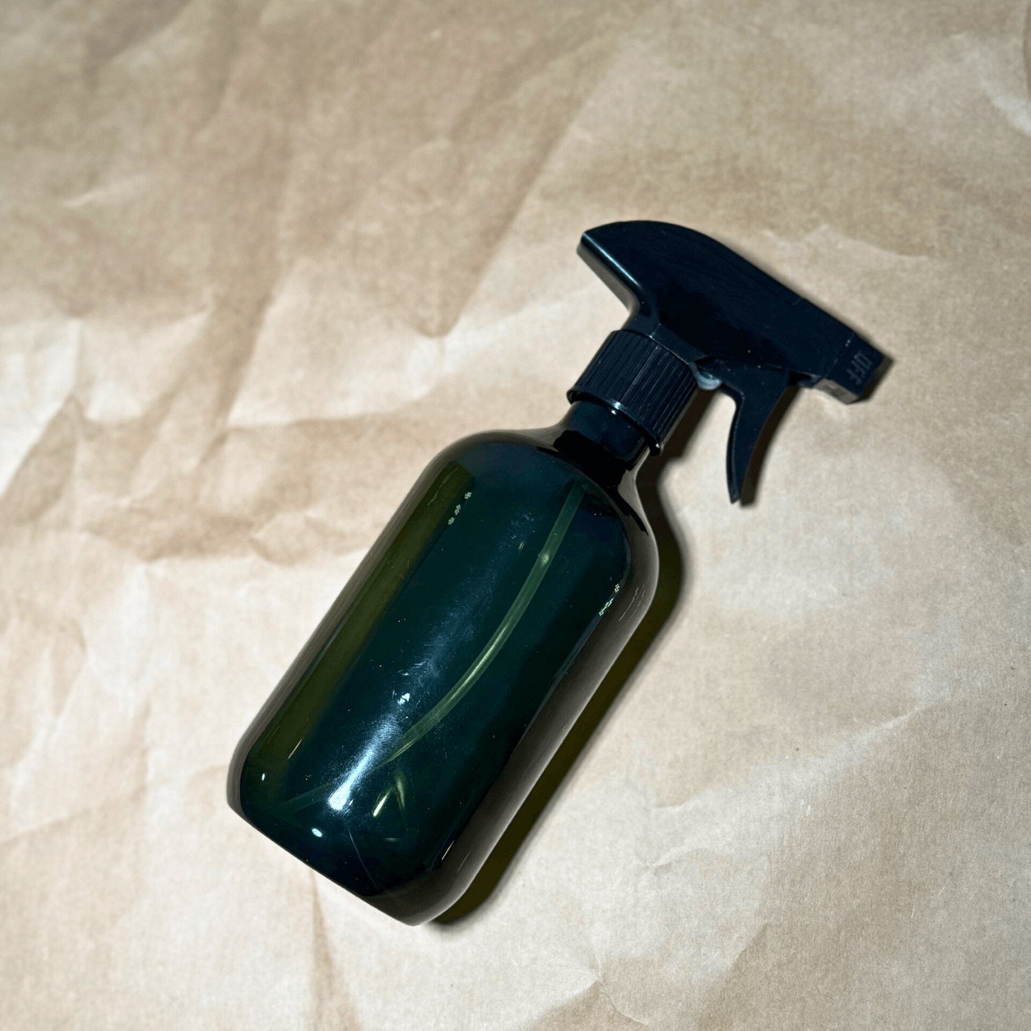 Green spray bottle for indoor plant care on neutral background, tool for misting houseplants and leaf cleaning